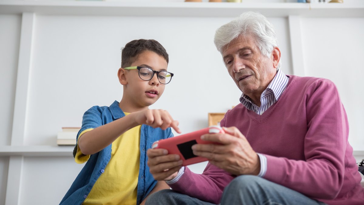 Senior man and young boy enjoying video games together indoors, fostering multi-generational connection.