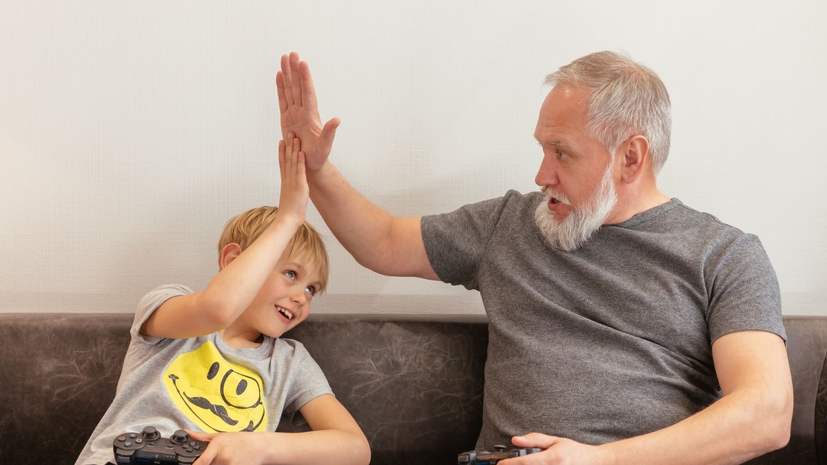Grandfather and grandson having fun with video games and sharing a joyful high five.