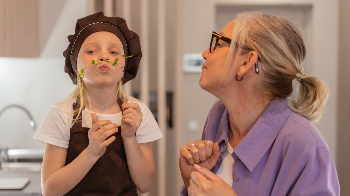 A grandmother and granddaughter share a playful moment in the kitchen, showcasing love and joy.