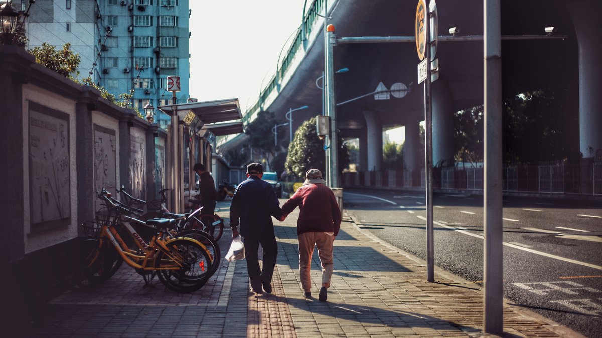 Senior couple holding hands walking along a sunny city sidewalk, embracing togetherness.