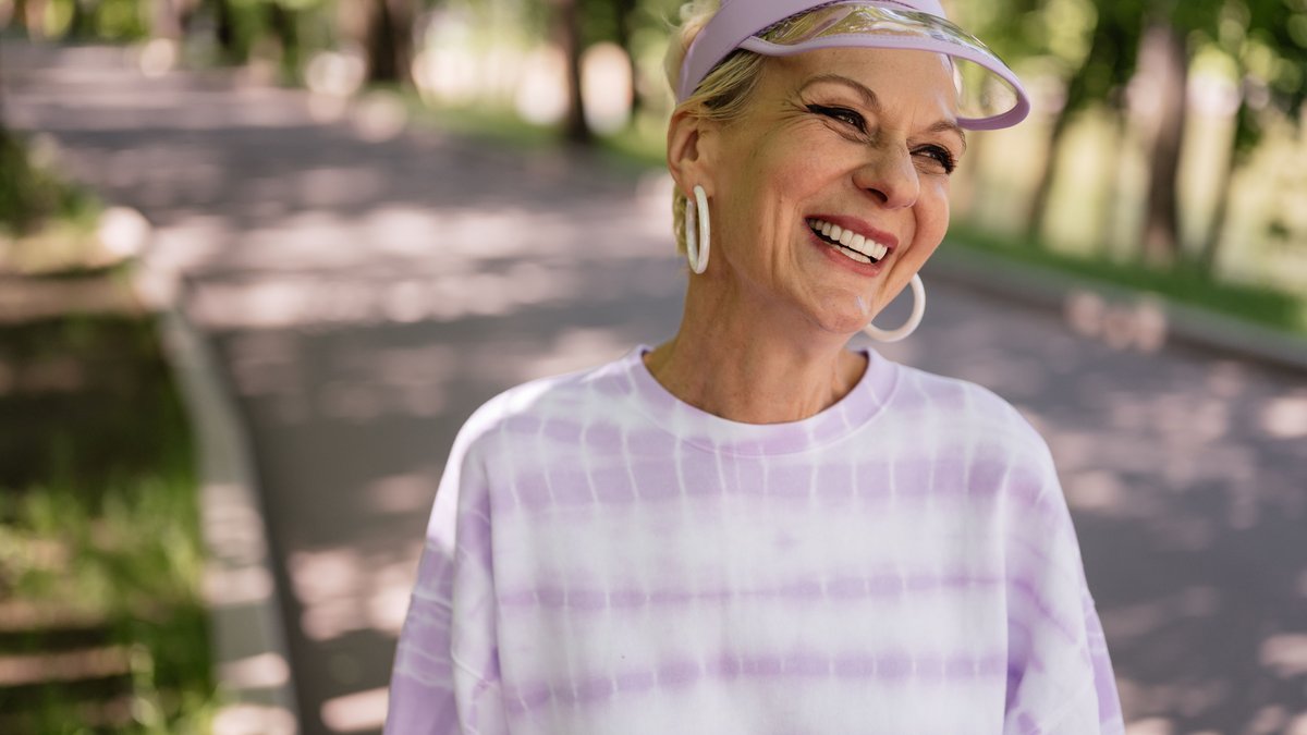 Smiling elderly woman enjoying a sunny day outdoors wearing a stylish sun visor.