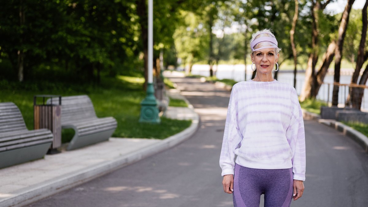 Senior woman in activewear enjoying a walk in a sunny park setting.