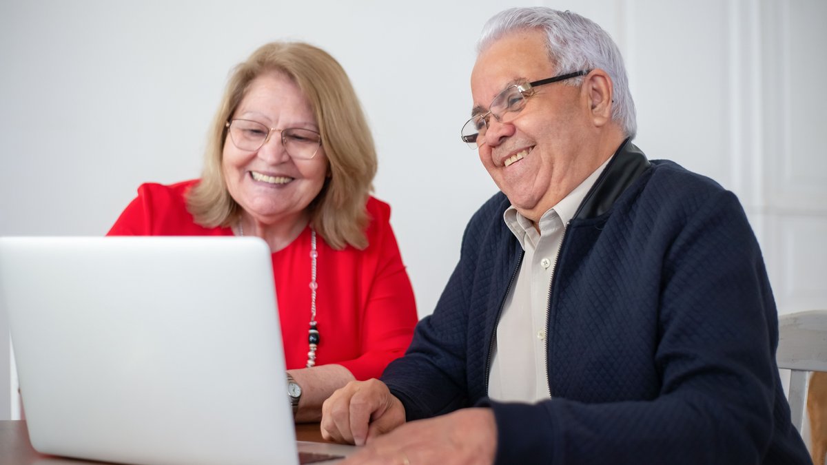 Elderly couple enjoying time together while using a laptop indoors, smiling and engaged.