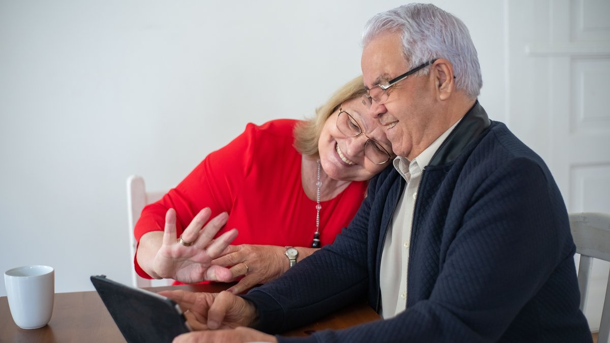 Happy senior couple enjoying a video call together on a tablet in a cozy indoor setting.