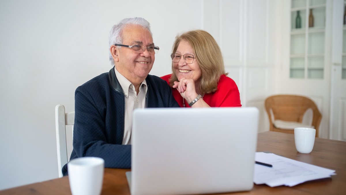 Senior couple smiling while using a laptop at home, enjoying online activities together.
