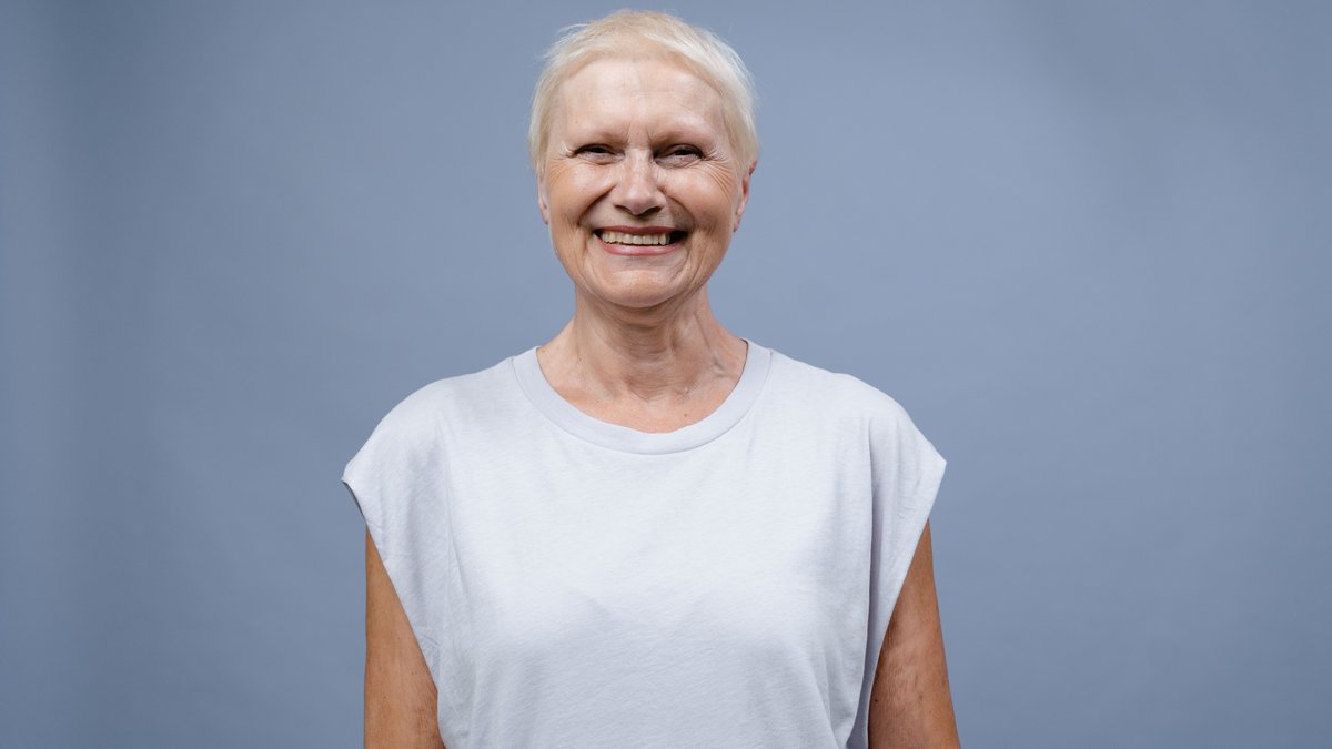 A joyful senior woman smiling warmly in a simple portrait against a blue backdrop.
