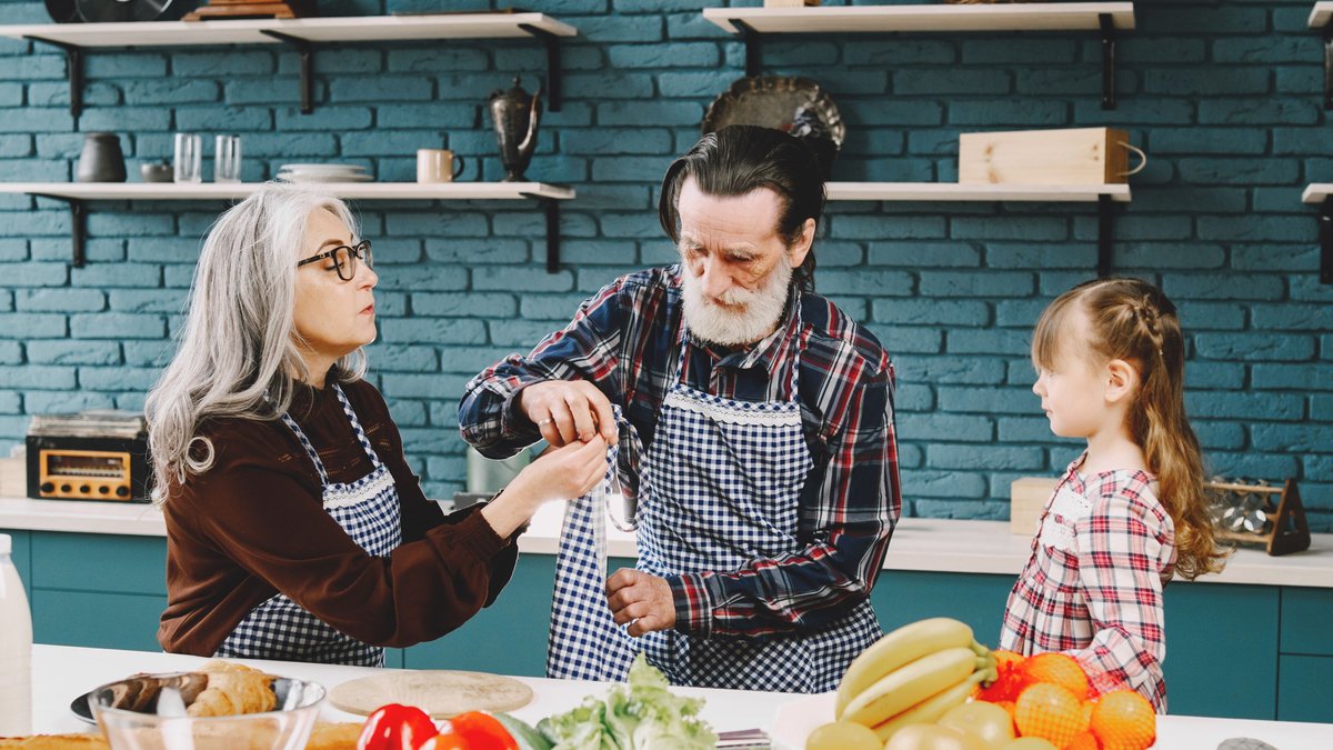 Senior couple and grandchild bonding over cooking in a cozy kitchen setting, enjoying quality time together.