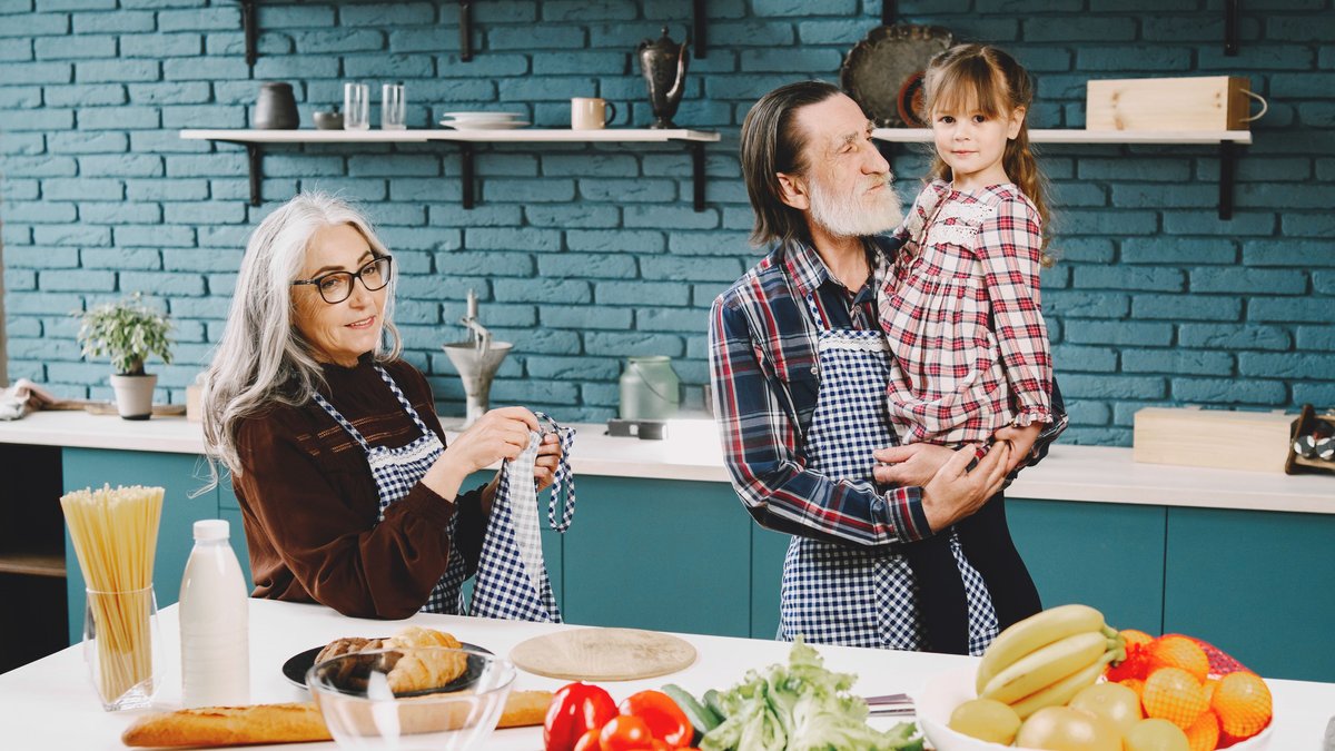 A joyful family scene in a modern kitchen with grandparents and grandchild cooking together.