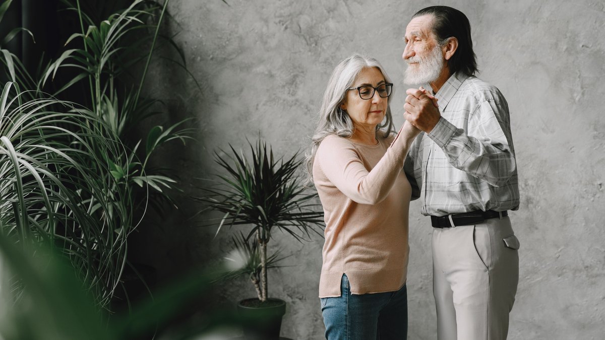 Joyful elderly couple dancing together in a cozy indoor garden, celebrating love and companionship.