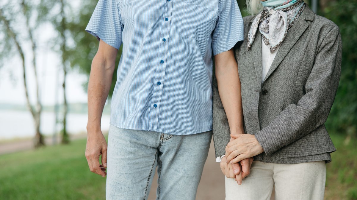 A senior couple enjoys a peaceful walk, holding hands in a serene park setting.