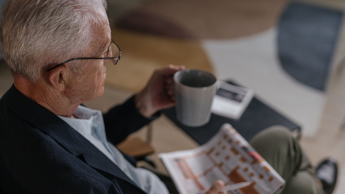 Senior man enjoying coffee while reading a newspaper indoors, exuding calm and relaxation.
