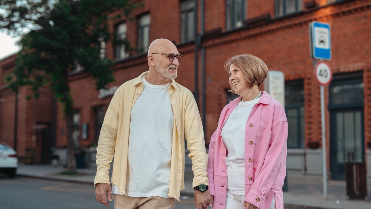 Elderly couple walking outside, holding hands with joyful expressions. Perfect for lifestyle themes.