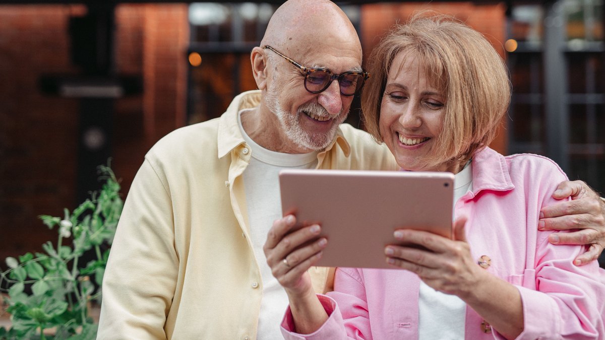 Happy senior couple using a tablet together, enjoying outdoor leisure time.