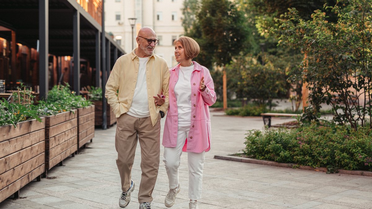 Happy senior couple walking together in a lush outdoor urban setting.