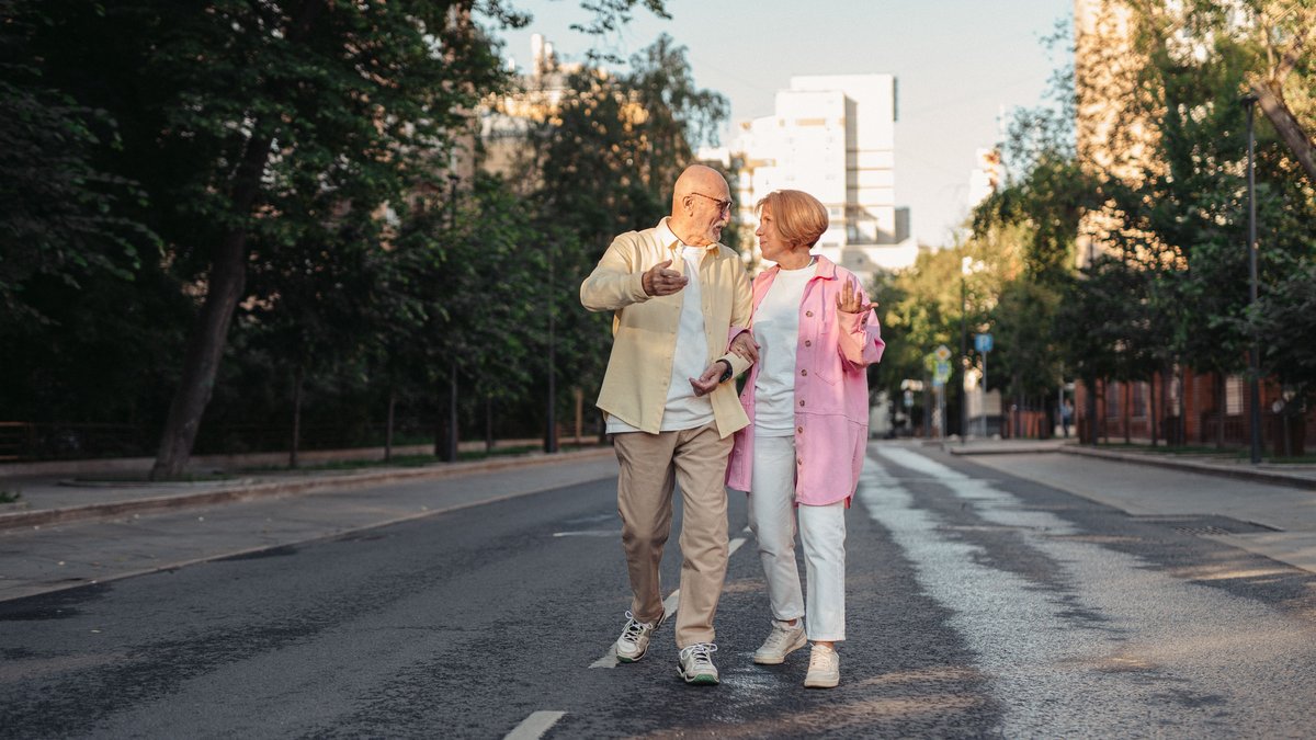 Happy elderly couple strolling down a sunny city street, enjoying a warm day outdoors.
