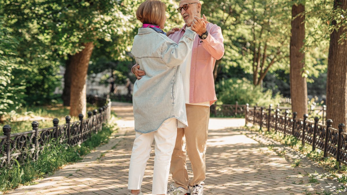 A joyful elderly couple dancing outdoors, showcasing love and happiness in a sunlit park.